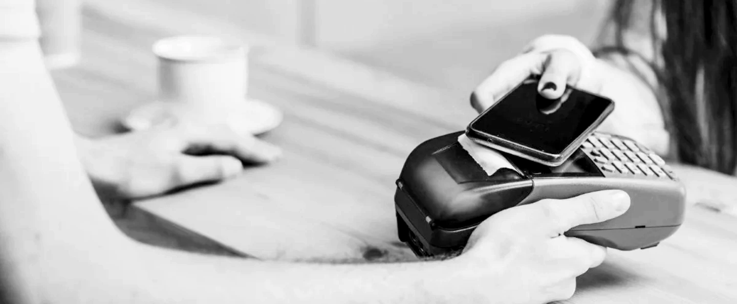 Una persona acerca su teléfono celular a una terminal de pago en el mostrador de un comercio