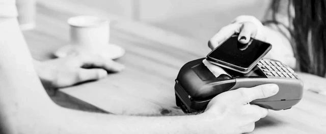 Una persona acerca su teléfono celular a una terminal de pago en el mostrador de un comercio